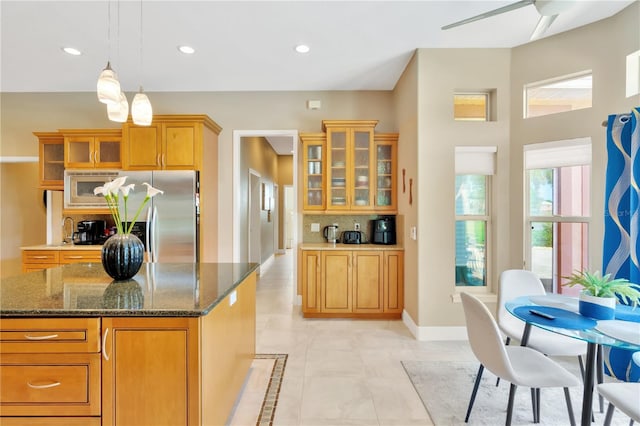 kitchen featuring stainless steel appliances, a center island, light tile flooring, dark stone counters, and ceiling fan