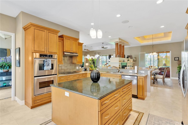 kitchen with kitchen peninsula, hanging light fixtures, appliances with stainless steel finishes, dark stone counters, and a center island