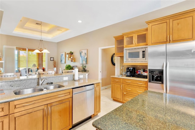 kitchen with hanging light fixtures, stainless steel appliances, sink, and light stone counters