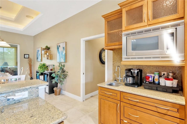 kitchen with light tile floors, sink, backsplash, stainless steel microwave, and light stone counters