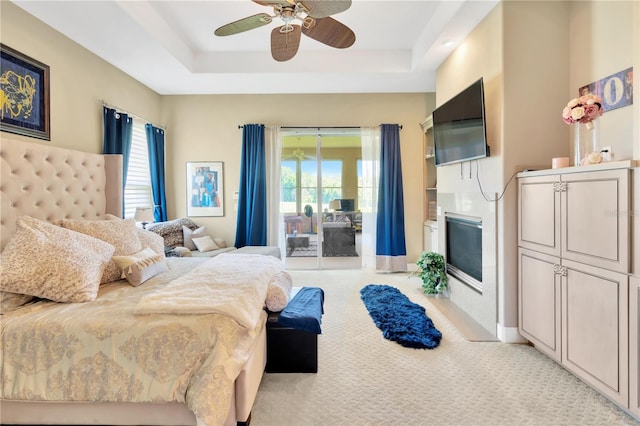 carpeted bedroom with access to exterior, ceiling fan, and a raised ceiling