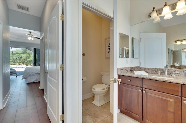 bathroom featuring toilet, vanity with extensive cabinet space, hardwood / wood-style floors, and ceiling fan