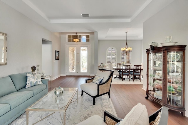 living room featuring a tray ceiling, french doors, a chandelier, and hardwood / wood-style flooring