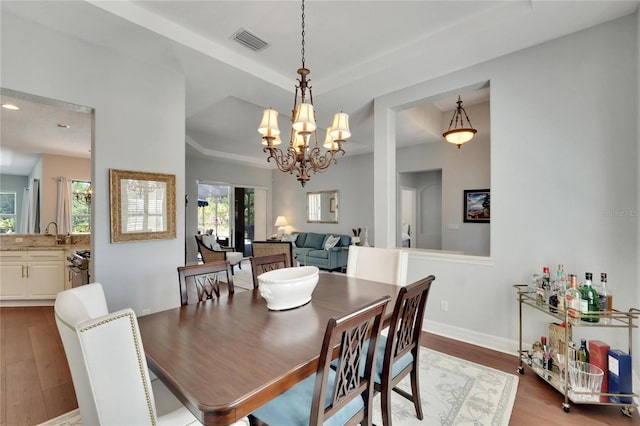 dining area featuring a notable chandelier, hardwood / wood-style floors, a tray ceiling, and sink