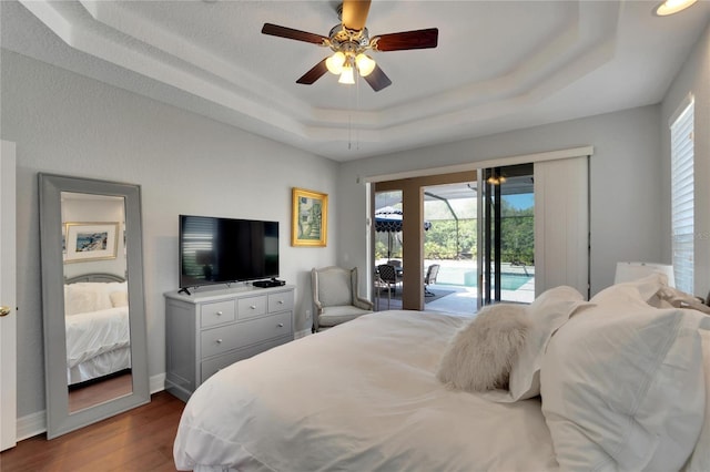 bedroom featuring a tray ceiling, access to outside, hardwood / wood-style floors, and ceiling fan