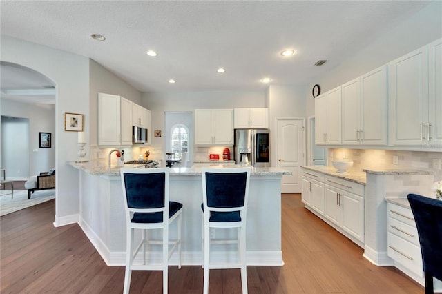 kitchen featuring light stone countertops, stainless steel appliances, light hardwood / wood-style flooring, white cabinets, and tasteful backsplash