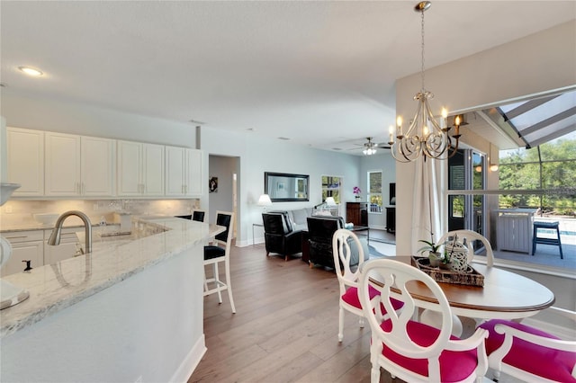 dining area featuring sink, ceiling fan with notable chandelier, vaulted ceiling, and light hardwood / wood-style flooring