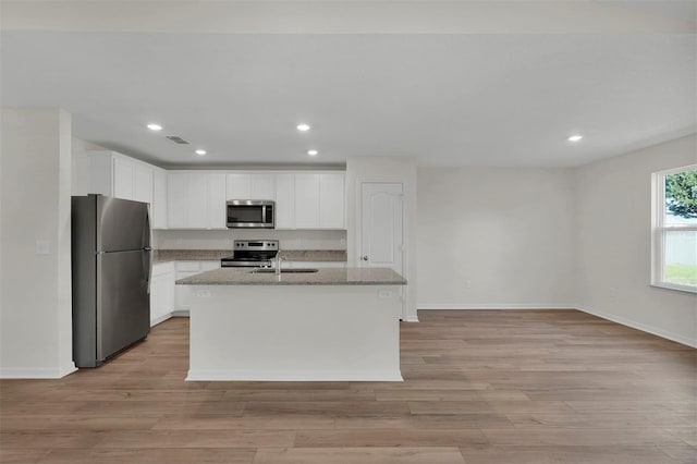 kitchen featuring light wood-type flooring, light stone countertops, a kitchen island with sink, and appliances with stainless steel finishes