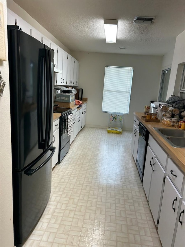 kitchen with white cabinets, black appliances, custom range hood, sink, and a textured ceiling