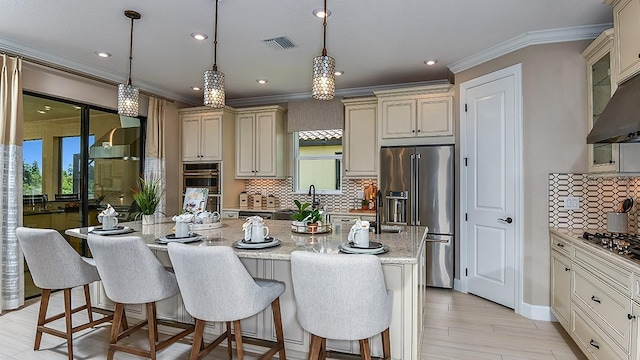 kitchen featuring appliances with stainless steel finishes, hanging light fixtures, light stone countertops, and an island with sink