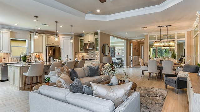 living room with a chandelier, a tray ceiling, light hardwood / wood-style floors, and crown molding