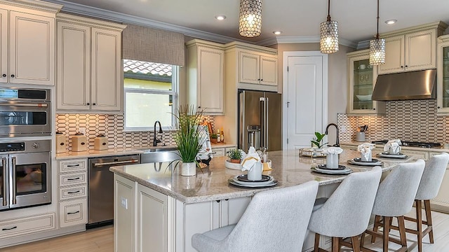 kitchen with tasteful backsplash, a center island with sink, cream cabinetry, and appliances with stainless steel finishes