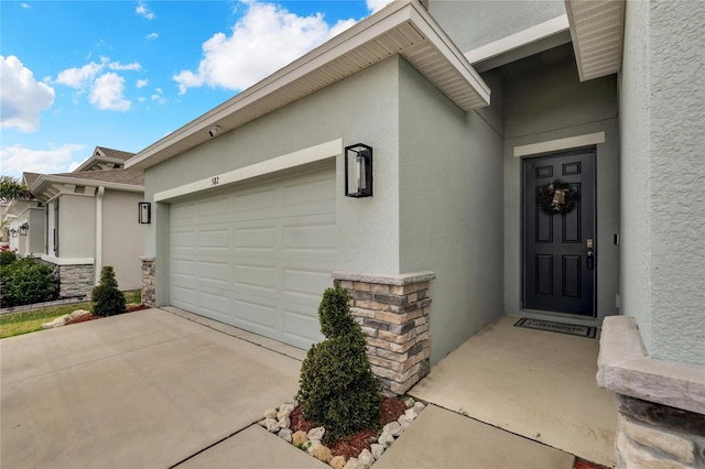 property entrance featuring a garage, stone siding, concrete driveway, and stucco siding