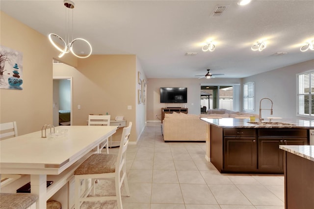 kitchen with light tile patterned floors, a sink, dark brown cabinetry, light stone countertops, and ceiling fan with notable chandelier