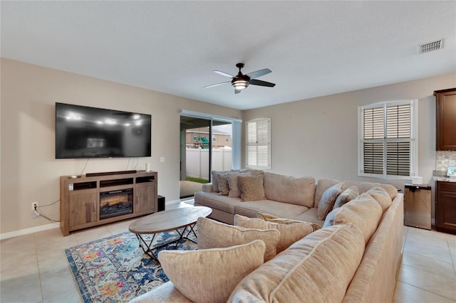 living room featuring light tile patterned floors, a glass covered fireplace, visible vents, and a ceiling fan