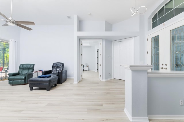 living area with high vaulted ceiling, light hardwood / wood-style floors, and ceiling fan with notable chandelier