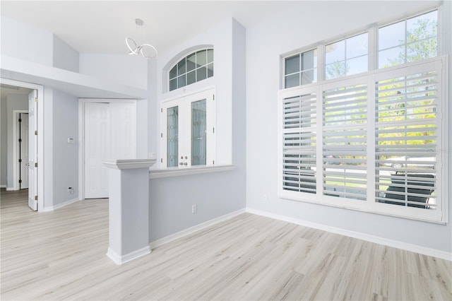 spare room featuring a notable chandelier, a towering ceiling, and light hardwood / wood-style flooring