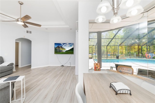 workout area with a pool, light hardwood / wood-style floors, ceiling fan with notable chandelier, and a tray ceiling