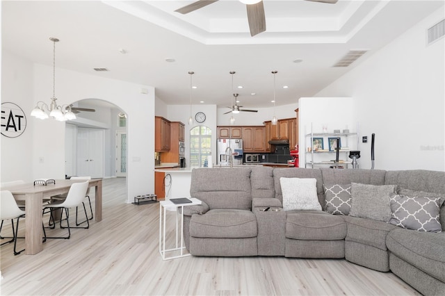 living room with a tray ceiling, light wood-type flooring, and ceiling fan with notable chandelier