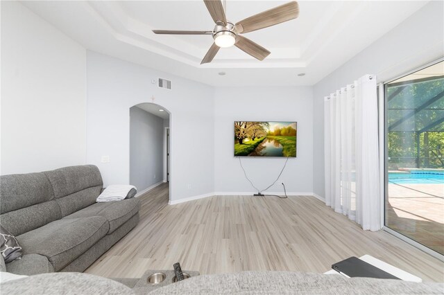 living room featuring a raised ceiling, ceiling fan, and light wood-type flooring