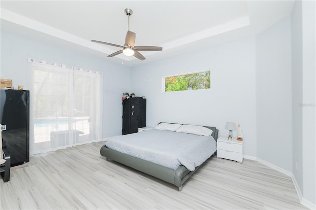 bedroom featuring a raised ceiling, ceiling fan, light wood-type flooring, and black fridge