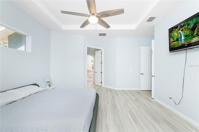 bedroom with a raised ceiling, ensuite bath, light hardwood / wood-style floors, and ceiling fan