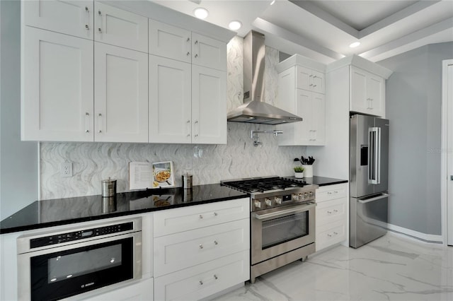 kitchen featuring white cabinets, light tile flooring, premium appliances, backsplash, and wall chimney range hood