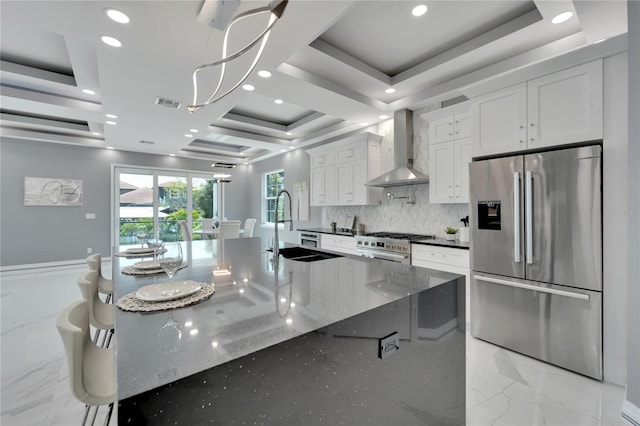 kitchen featuring appliances with stainless steel finishes, wall chimney exhaust hood, white cabinetry, a tray ceiling, and dark stone countertops