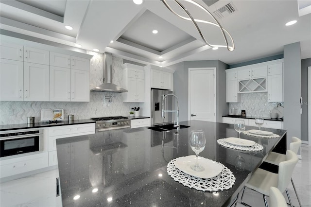 kitchen featuring appliances with stainless steel finishes, backsplash, wall chimney exhaust hood, and white cabinetry