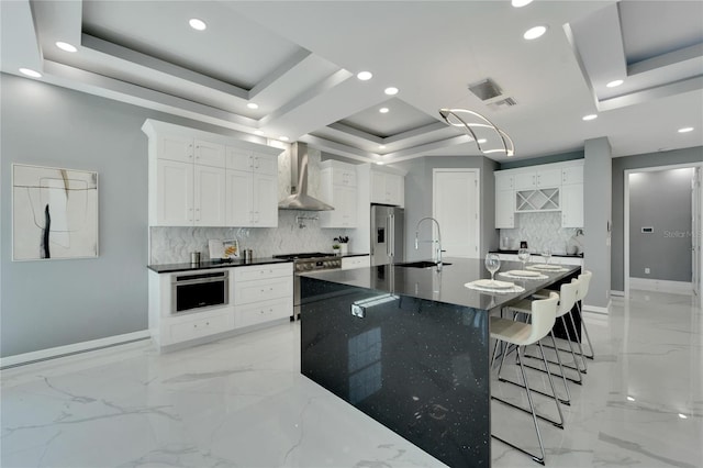 kitchen with premium appliances, white cabinetry, wall chimney range hood, a raised ceiling, and tasteful backsplash