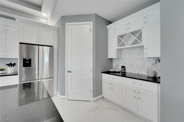 kitchen with stainless steel refrigerator with ice dispenser, tasteful backsplash, dark stone countertops, white cabinets, and light tile floors