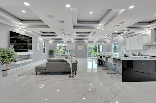 kitchen with wall chimney exhaust hood, light tile floors, white cabinets, a kitchen bar, and backsplash