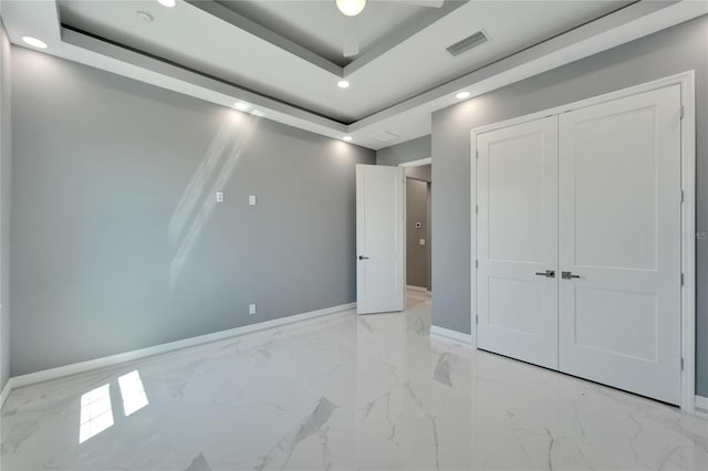 unfurnished bedroom with a tray ceiling, a closet, and light tile flooring