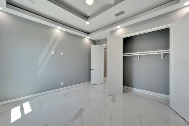 unfurnished bedroom featuring a closet, ceiling fan, a tray ceiling, and light tile flooring