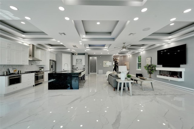 kitchen featuring tasteful backsplash, wall chimney range hood, white cabinets, and a raised ceiling