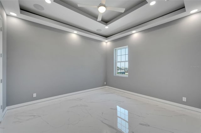 tiled empty room featuring ceiling fan and a raised ceiling