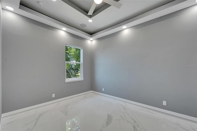 spare room featuring ceiling fan, a tray ceiling, and light tile floors