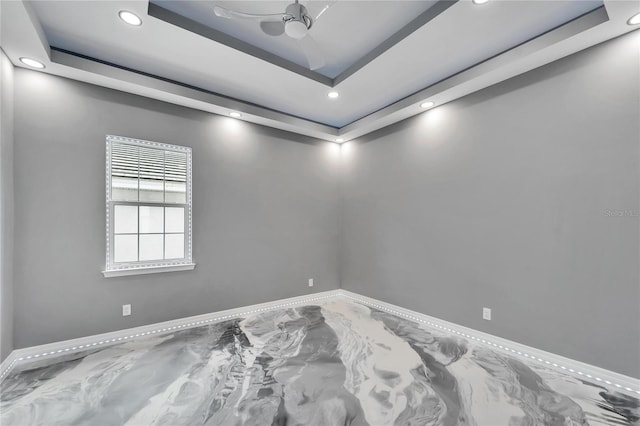 unfurnished room with ceiling fan and a tray ceiling