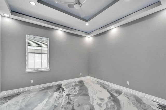 empty room with ceiling fan and a tray ceiling