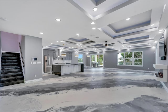 unfurnished living room with a raised ceiling, coffered ceiling, and ceiling fan