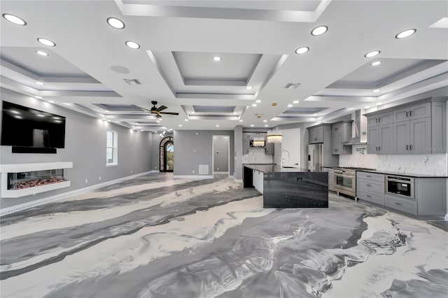 interior space featuring hanging light fixtures, wall chimney range hood, ceiling fan, backsplash, and gray cabinets