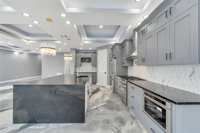 kitchen featuring tasteful backsplash, pendant lighting, a tray ceiling, and a center island with sink