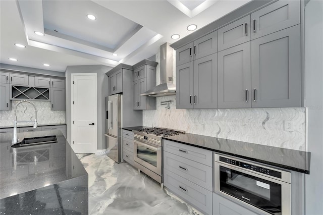 kitchen with a tray ceiling, tasteful backsplash, high end appliances, and wall chimney exhaust hood