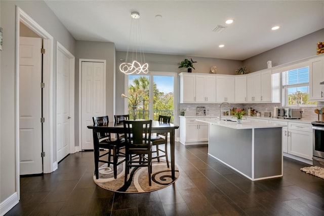 kitchen featuring hanging light fixtures, a notable chandelier, white cabinets, a center island with sink, and tasteful backsplash