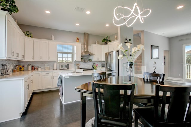 kitchen with decorative light fixtures, backsplash, stainless steel fridge with ice dispenser, a kitchen bar, and wall chimney exhaust hood