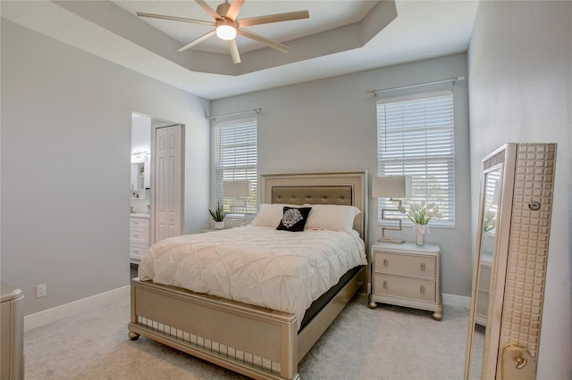 carpeted bedroom with ensuite bath, ceiling fan, and a tray ceiling