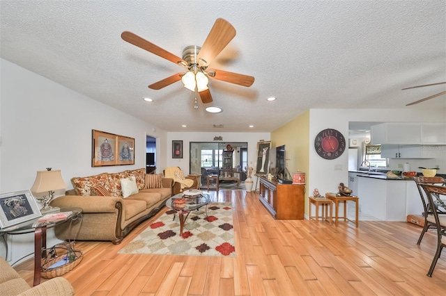 living room with a textured ceiling, light wood-type flooring, ceiling fan, and sink