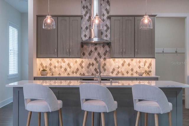 kitchen featuring pendant lighting, dark hardwood / wood-style floors, a center island with sink, and wall chimney range hood