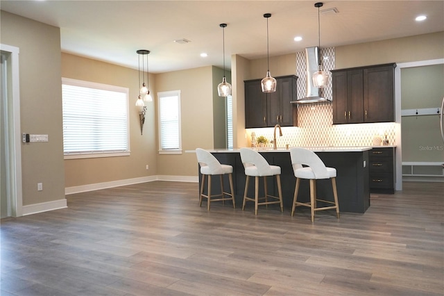 kitchen with dark brown cabinetry, wall chimney exhaust hood, a kitchen breakfast bar, dark hardwood / wood-style floors, and pendant lighting