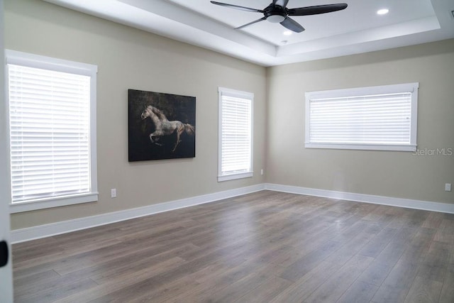 empty room with dark wood-type flooring, a raised ceiling, and ceiling fan